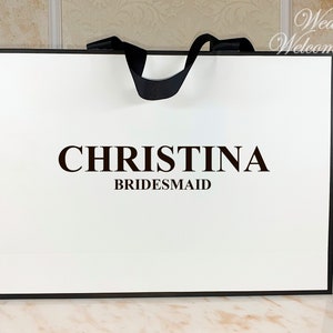 May include: White gift bag with black handles and a black border. The bag has the text "CHRISTINA BRIDESMAID" printed on the front.