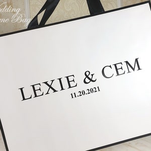 May include: White wedding welcome bag with black handles and black text that reads "Lexie & Cem 11.20.2021".