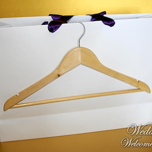 May include: White paper gift bag with purple ribbon handles and a wooden hanger inside. The bag has the text "Wedding Welcome Bag" printed on the bottom.