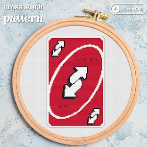 Puede incluir: Patrón de punto de cruz con una carta roja de Uno con flechas blancas y el texto "Love you more". El diseño está en un bastidor de bordado de madera sobre un fondo azul claro.