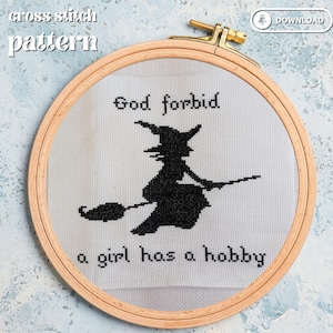 Op de afbeelding: Kruissteekpatroon in een houten borduurring met een zwart silhouet van een heks op een bezem. De tekst luidt "God forbid a girl has a hobby". De achtergrond is een lichtblauw en wit patroon.