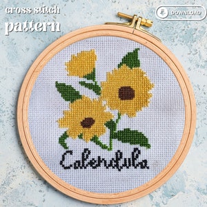 May include: A cross-stitch pattern of yellow calendula flowers with green leaves, stitched on white fabric, set in a wooden embroidery hoop. The word "Calendula" is stitched in black script below the flowers. The words "cross stitch pattern" are at the top.
