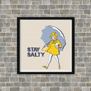 Puede incluir: Un patr&oacute;n de punto de cruz con una ni&ntilde;a con un impermeable amarillo sosteniendo una sombrilla azul. El texto "STAY SALTY" est&aacute; escrito en negro debajo de la ni&ntilde;a.