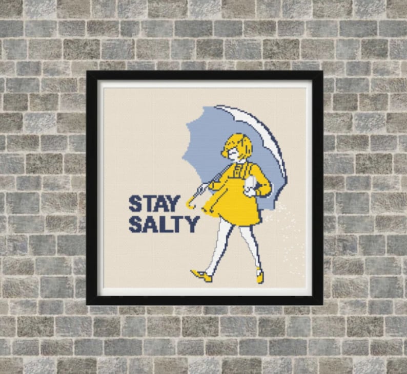 Puede incluir: Un patr&oacute;n de punto de cruz con una ni&ntilde;a con un impermeable amarillo sosteniendo una sombrilla azul. El texto "STAY SALTY" est&aacute; escrito en negro debajo de la ni&ntilde;a.