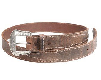 May include: A brown leather belt with a silver buckle featuring an engraved design. The belt has white stitching and is rolled up.