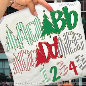 May include: A white fabric with a Christmas-themed alphabet and numbers design. The letters and numbers are in green, red, and black, with striped and solid patterns. The design includes Christmas trees and stars.