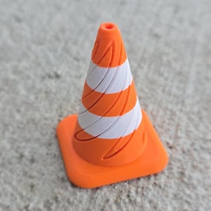 May include: A small orange and white traffic cone with a spiral pattern. The cone is made of plastic and has a flat base.