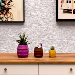 Op de afbeelding: Een houten bureau met twee witte lades en een bruin blad. Op het bureau staan een potplant, een pennenhouder en een kleine cactus. Boven het bureau hangen twee ingelijste kunstwerken, waarvan één met een ananas.