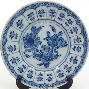 Könnte beinhalten: Ein blauer und weißer Delft-Teller mit einem Blumendesign. Der Teller hat einen gewellten Rand und ist mit einem sich wiederholenden Muster aus stilisierten Blumen verziert.