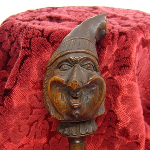 May include: A wooden nutcracker in the shape of a jester's head with a wide grin and a tall, pointed hat. The nutcracker is carved with intricate details and has a dark brown finish.