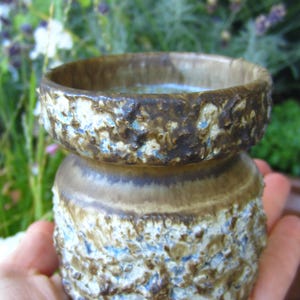 May include: A brown and white ceramic planter with a textured surface. The planter has a wide, round top and a narrower base.