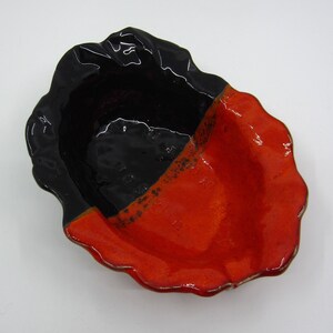 May include: A black and orange ceramic dish with a scalloped edge. The dish is glazed and has a glossy finish.