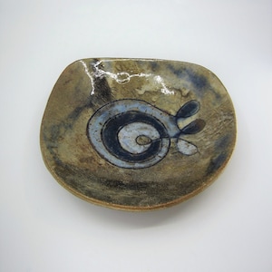 May include: A small, oval-shaped ceramic dish with a brown, blue, and white abstract design. The dish has a glossy glaze and a slightly raised rim.