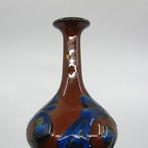May include: A small, brown ceramic vase with blue and green floral designs. The vase has a narrow neck and a rounded body.