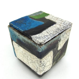 Peut inclure: Une boîte carrée en céramique avec un couvercle. La boîte est décorée d'un glaçage craquelé dans des tons de blanc, noir, bleu et vert.