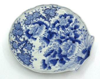 May include: A white ceramic plate with a blue and white floral design. The plate is shaped like a seashell and has a scalloped edge.