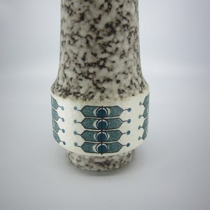 Op de afbeelding: Een witte keramische vaas met een gespikkeld bruin glazuur en een blauw en wit geometrisch patroon rond het midden.