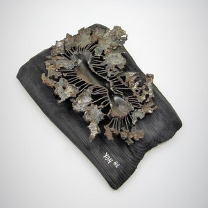 May include: A metal sculpture of a stylized flower with a rusty finish, mounted on a dark wood plaque. The plaque is signed "YOH 82".