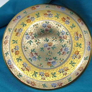 Puede incluir: Un plato dorado con un diseño floral. El plato está decorado con un patrón de pequeñas flores y hojas de colores.