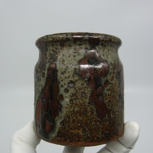 May include: A small, brown ceramic pot with a speckled glaze. The pot has a rounded shape and a wide mouth.