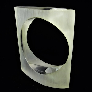 以下が含まれることがあります： 中央に円形の開口部を持つ、白い曲線的な幾何学的な彫刻。彫刻は滑らかで磨かれた素材で作られており、控えめな光沢があります。