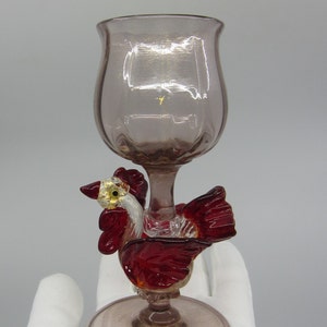 以下が含まれることがあります： ベースに赤と白のガラス製の雄鶏が取り付けられたガラス製のゴブレット。ゴブレットは薄いピンク色です。