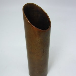 Pode incluir: Um vaso de cor cobre com uma abertura ligeiramente oval. O vaso é feito de um material metálico liso e tem um aspecto ligeiramente envelhecido.