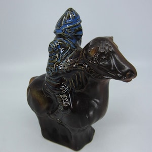 Puede incluir: Una figurita de cerámica de un caballero montando un caballo. El caballero lleva una armadura azul y marrón y un casco. El caballo es marrón y tiene una crin y una cola detalladas.