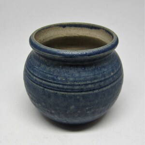 May include: A small, round, blue ceramic pot with a speckled glaze and a white rim. The pot has three horizontal lines around the middle.