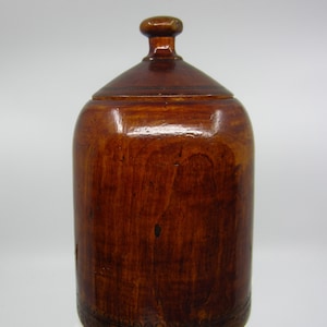 May include: A wooden jar with a lid and a decorative band around the bottom. The jar is a dark brown color and has a smooth, polished finish.