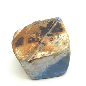 Puede incluir: Una escultura de cerámica abstracta y artesanal, con una forma angular única. La pieza presenta una mezcla de colores, incluyendo marrón, azul y blanco, con una superficie texturizada. El diseño de la escultura es moderno y artístico, para la decoración del hogar.