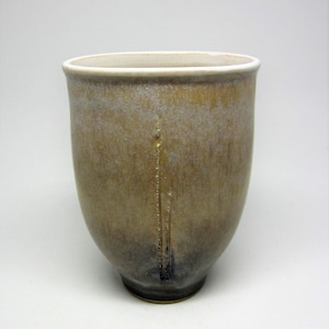 Könnte beinhalten: Eine braune Keramiktasse mit weißem Rand und einer subtilen Glasurvariation. Die Tasse hat eine abgerundete Form und eine leicht ausgestellte Lippe.