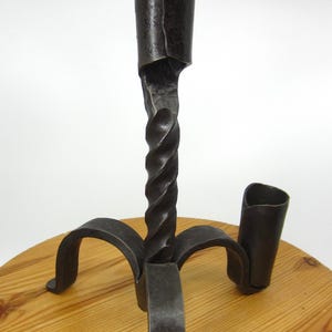 May include: A black metal candlestick with a twisted stem and three legs. The candlestick has a single candle holder and a smaller side holder.