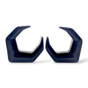Könnte beinhalten: Zwei dunkelblaue, geometrisch geformte Ohrringe. Jeder Ohrring hat eine Fünfeckform mit einer spitzen Oberseite und einer gebogenen Öffnung. Die Ohrringe sind vor weißem Hintergrund dargestellt.