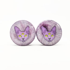 May include: A pair of purple and white ear gauges featuring a three-eyed cat design.