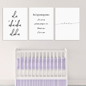 May include: Three white framed prints with black calligraphy on a white wall above a white crib with a lavender mattress and skirt. The prints read "ola 'aka'aka aloha", "ho'oponopono I'm sorry please forgive me thank you I love you", and "aloha".