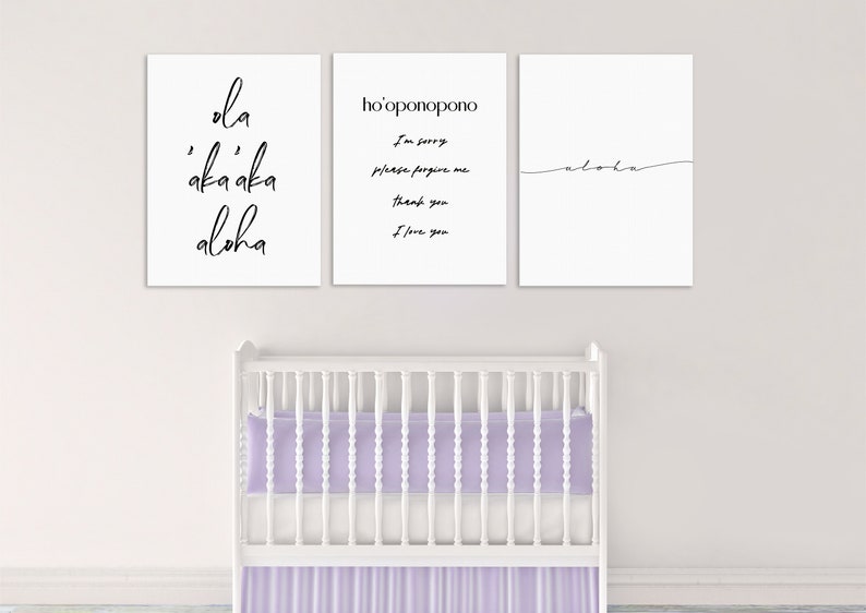 May include: Three white framed prints with black calligraphy on a white wall above a white crib with a lavender mattress and skirt. The prints read "ola 'aka'aka aloha", "ho'oponopono I'm sorry please forgive me thank you I love you", and "aloha".