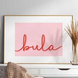 Może przedstawiać: Wydruk w ramie z różowym tłem i napisem "bula" napisanym czerwonym, ozdobnym pismem.