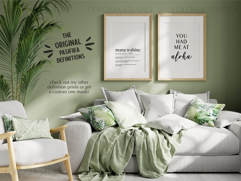 May include: Two framed prints with black text on a white background. The print on the left says "mana wahine" and the print on the right says "You had me at aloha". The prints are hanging on a sage green wall above a white couch with green throw pillows and a green throw blanket.