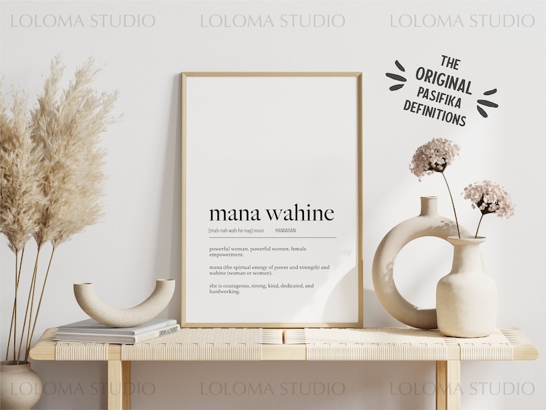 May include: A framed print with a white background and black text. The text reads "mana wahine" and defines the word as "powerful woman, powerful women, female empowerment". The print is on a wooden shelf with two ceramic vases and dried pampas grass.