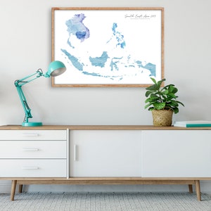 Peut inclure: Une impression aquarelle d'une carte de l'Asie du Sud-Est dans des tons bleus, encadr&eacute;e dans un cadre en bois clair. L'impression est accroch&eacute;e &agrave; un mur blanc au-dessus d'une commode blanche &agrave; trois tiroirs et une porte coulissante.