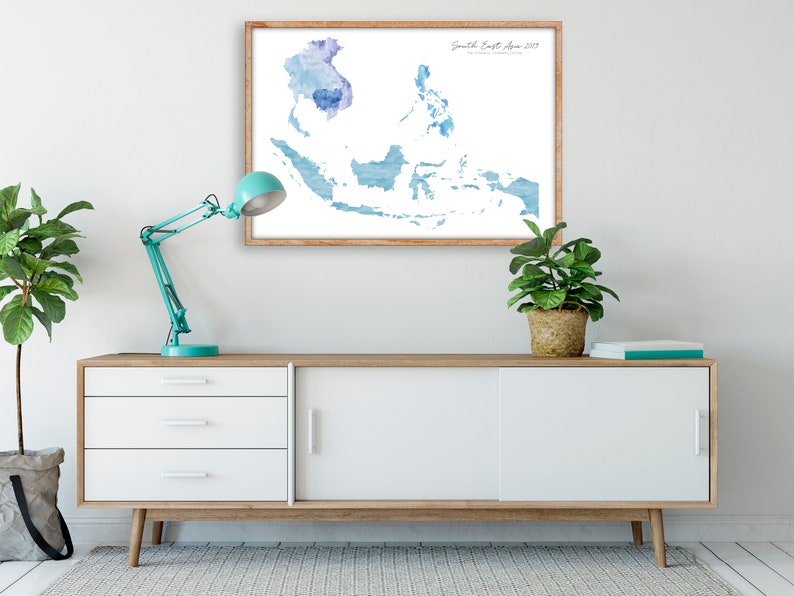 Peut inclure: Une impression aquarelle d'une carte de l'Asie du Sud-Est dans des tons bleus, encadr&eacute;e dans un cadre en bois clair. L'impression est accroch&eacute;e &agrave; un mur blanc au-dessus d'une commode blanche &agrave; trois tiroirs et une porte coulissante.