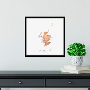 Puede incluir: Una impresi&oacute;n enmarcada de un mapa acuarela de Escocia con los nombres de las regiones etiquetados. El mapa est&aacute; en tonos naranja y rosa. El texto "Escocia" y "Donde todo comenz&oacute;" est&aacute; impreso debajo del mapa.