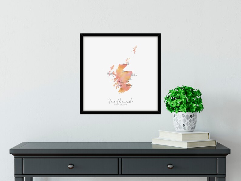 Puede incluir: Una impresi&oacute;n enmarcada de un mapa acuarela de Escocia con los nombres de las regiones etiquetados. El mapa est&aacute; en tonos naranja y rosa. El texto "Escocia" y "Donde todo comenz&oacute;" est&aacute; impreso debajo del mapa.