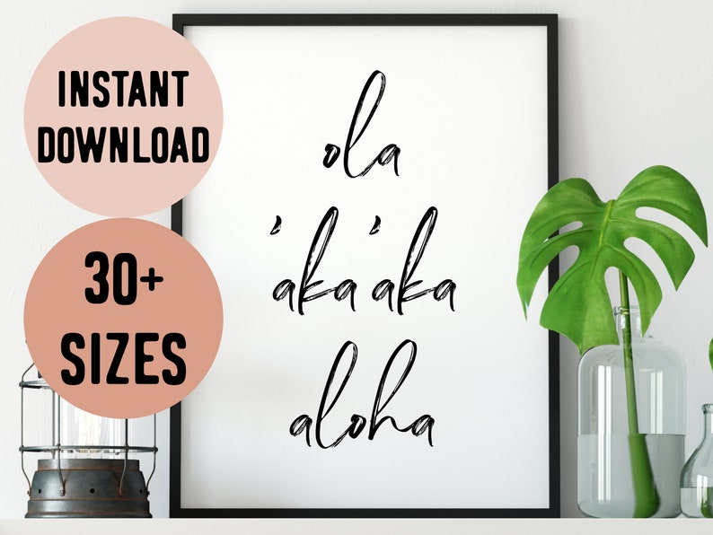 May include: A black and white printable wall art print with the text "ola 'aka 'aka aloha" in a cursive font. The print is framed in a black frame and is displayed on a white wall.
