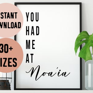 Könnte beinhalten: Ein schwarz-weißer druckbarer Wandkunstdruck mit dem Text "You had me at Noa'ia". Der Druck ist in einem schwarzen Rahmen gerahmt und wird an einer weißen Wand mit einer grünen Pflanze in einer durchsichtigen Glasvase ausgestellt.