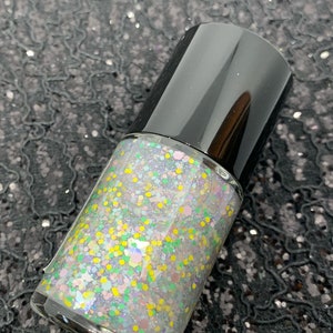 May include: A clear glass bottle of nail polish with a black cap. The polish is a light iridescent color with multi-colored glitter.
