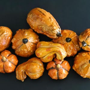 May include: An assortment of decorative gourds in shades of orange and brown, with diverse shapes and sizes. Some gourds have a textured surface and dark stems. The gourds are arranged on a dark background, creating a seasonal display.