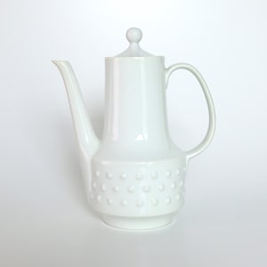 Könnte beinhalten: Weiße Kaffeekanne aus Keramik mit rundem Deckel und texturiertem Boden. Die Kanne hat einen Ausguss und einen Griff.