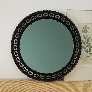 Op de afbeelding: Een ronde spiegel met een zwart frame en een zilveren decoratieve rand. De spiegel heeft een lichtblauwe tint.